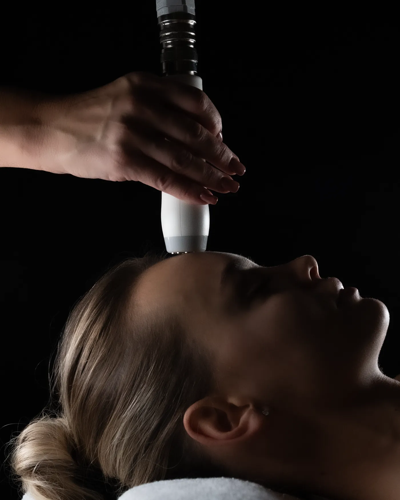A T-Shape 2 face handpiece held above a client's forehead as she rests, eyes closed