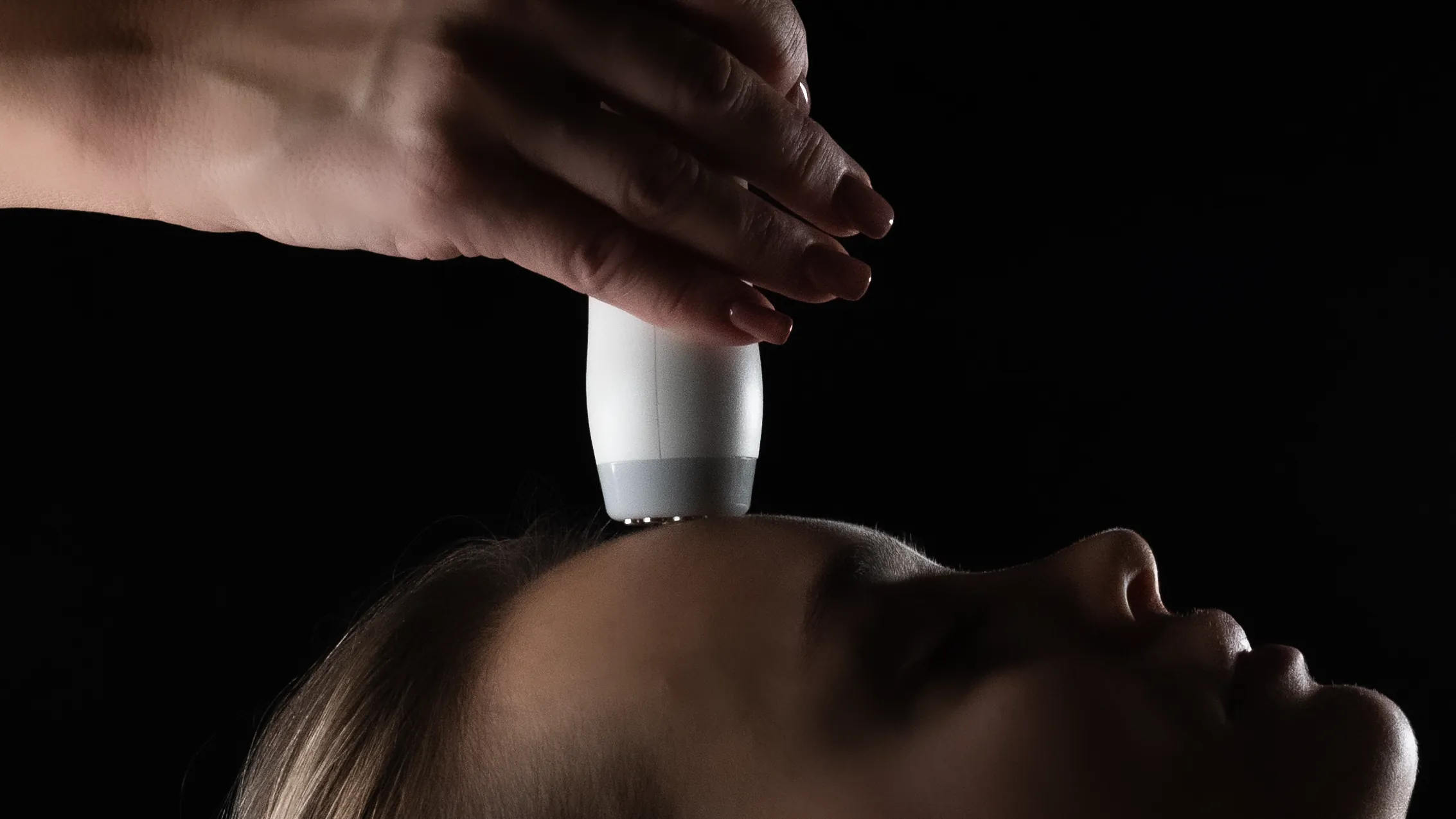 A T-Shape 2 face handpiece held just above a woman's forehead as she rests, eyes closed